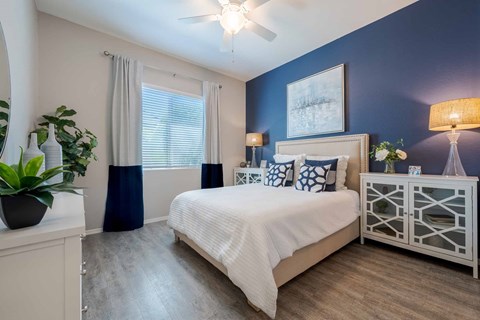 A bedroom with a bed, nightstand, and a plant. at Vistoria At Marley Park Apartments, Arizona