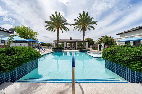 A swimming pool surrounded by palm trees and a blue sky. at Vistoria At Stadium Apartments, Glendale, AZ, 85305