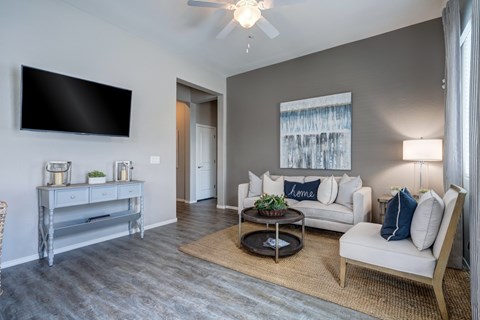 A living room with a white couch, a grey table, and a flat screen TV mounted on the wall.