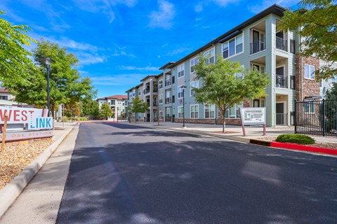 A street view of a residential area with apartment buildings and a sign that reads "WES LINK".