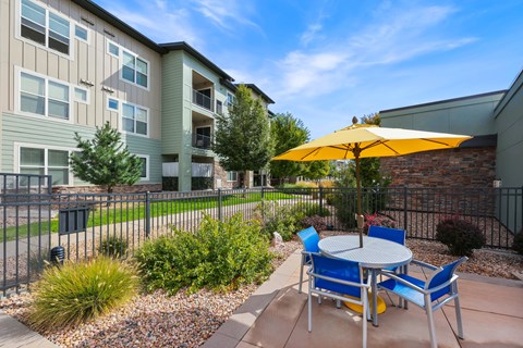 A patio with a table and chairs and a yellow umbrella.