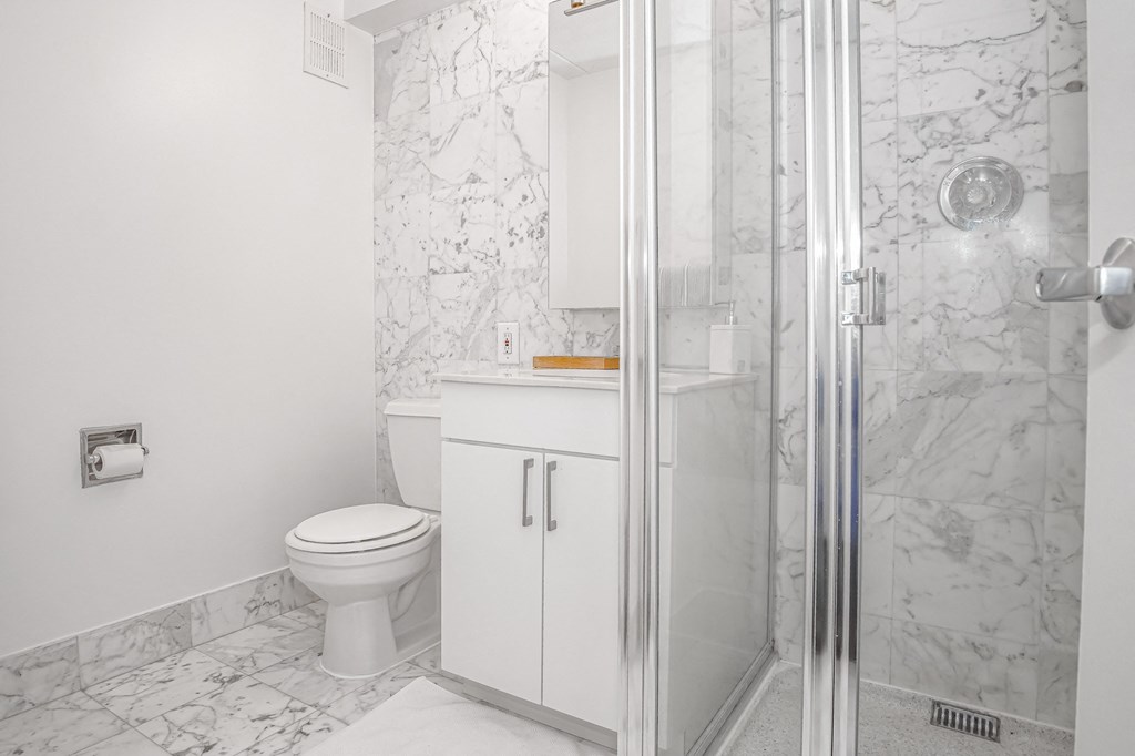 A bathroom with white cabinet and toilet and marble walls at 10 West Apartments, Long Beach, NY