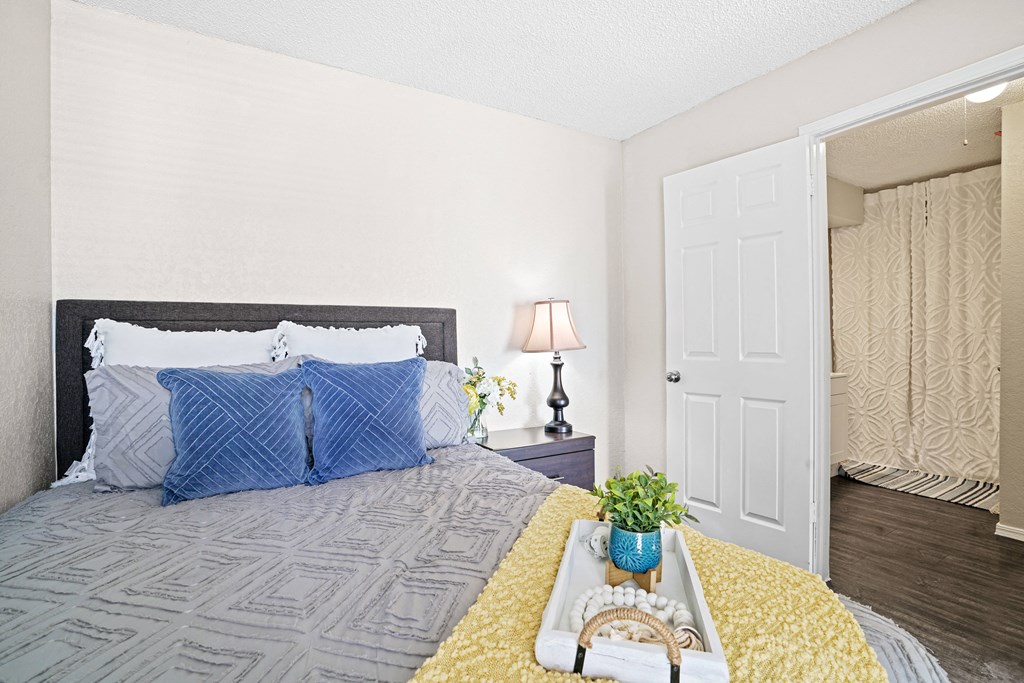 bedroom with yellow blanket on bed and blue pillows and blue paintingbedroom with yellow blanket on bed and blue pillows with view looking into bathroom