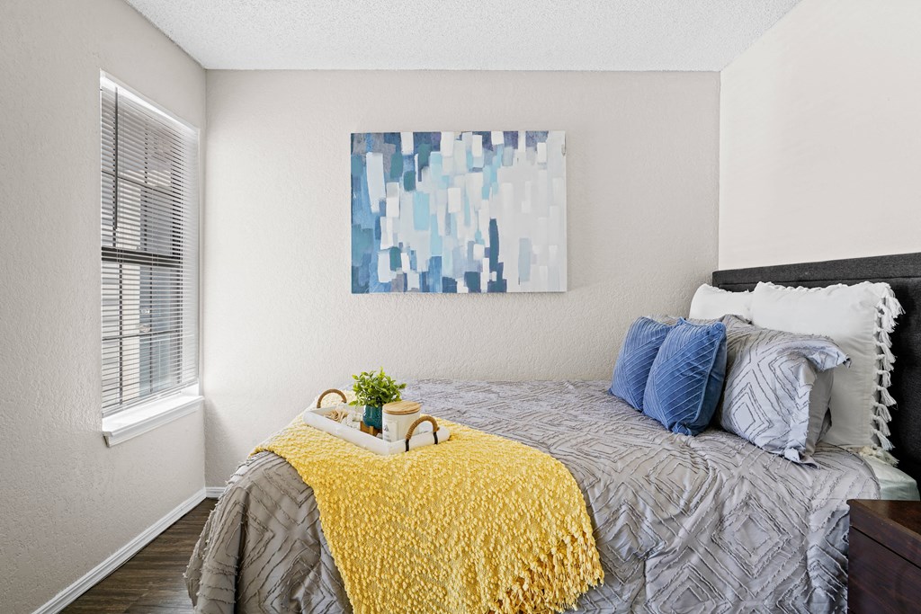 bedroom with yellow blanket on bed and blue pillows and blue painting
