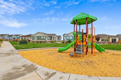 a playground with yellow mulch and houses in the background at The Villas at Prairie Center, Brighton