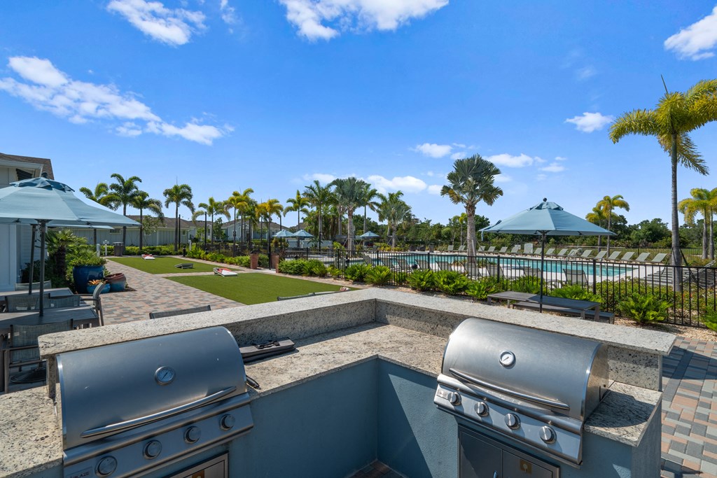 two bbqs on a patio overlooking a pool with palm trees at Artesia at Lakewood Ranch Apartments, Florida 34211