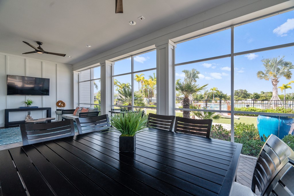 a patio with a wooden table and chairs and large windows at Artesia at Lakewood Ranch Apartments, Bradenton, FL