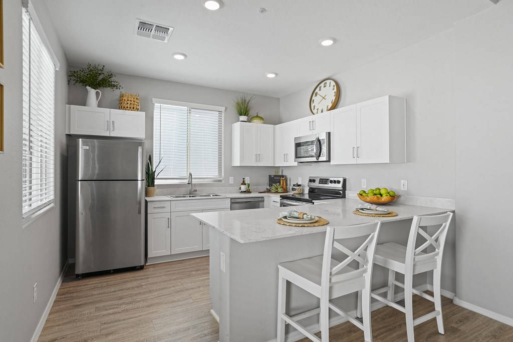 a kitchen with white cabinets and a white island with two stools at Sienna at South Mountain Apartments, Laveen, AZ