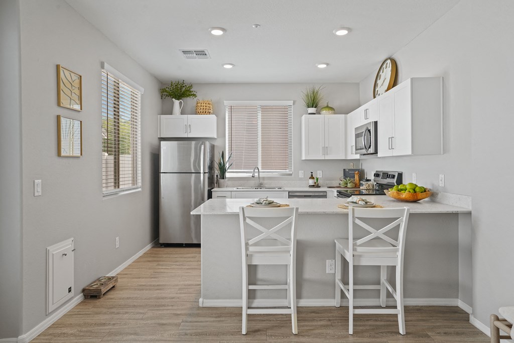 a kitchen with white cabinets and a white island with stools at Sienna at South Mountain Apartments, Laveen, 85339