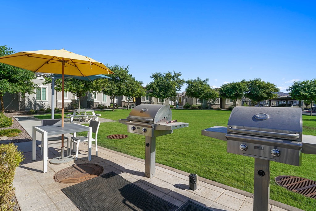 a patio with two bbq grills and a table with an umbrella at Sienna at South Mountain Apartments, Laveen, Arizona