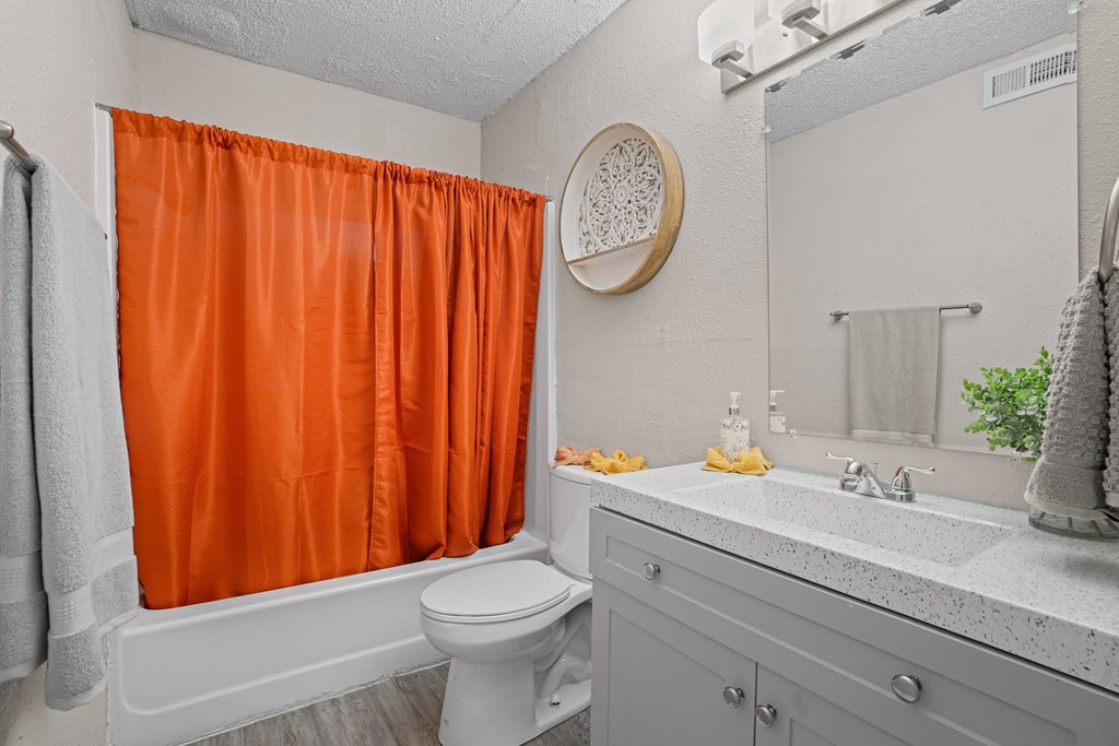a bathroom with an orange shower curtain and a toilet and a sink