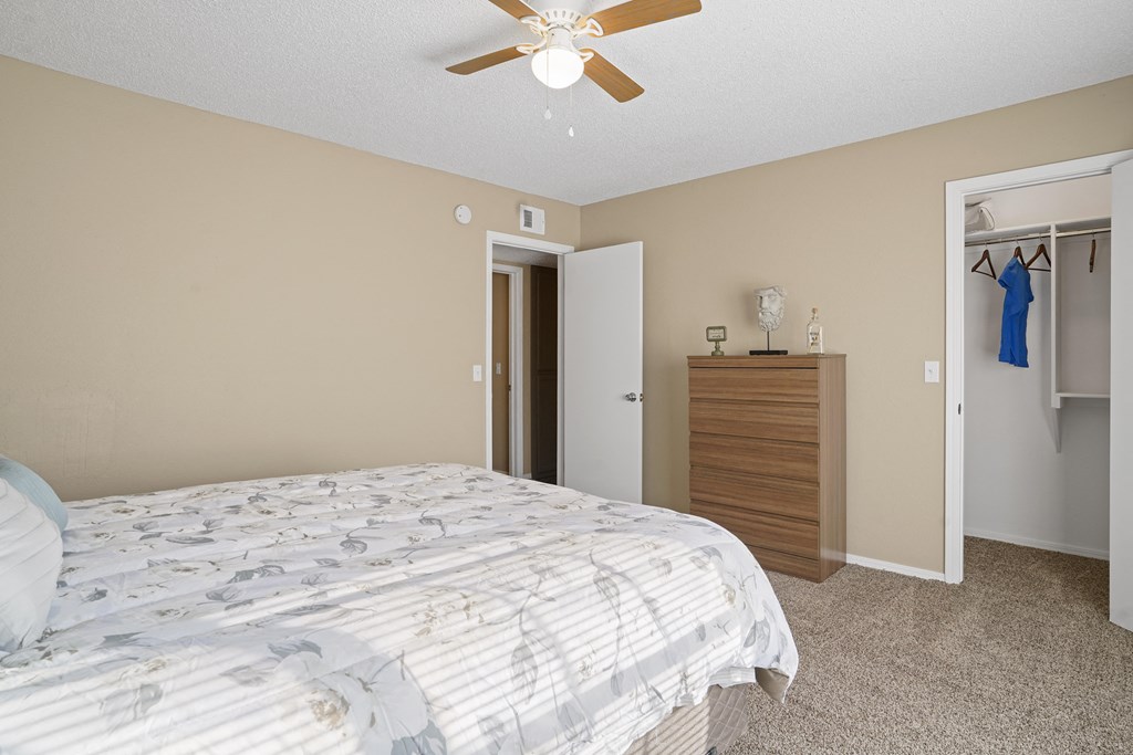 bedroom with white blanket on bed, ceiling fan and closet