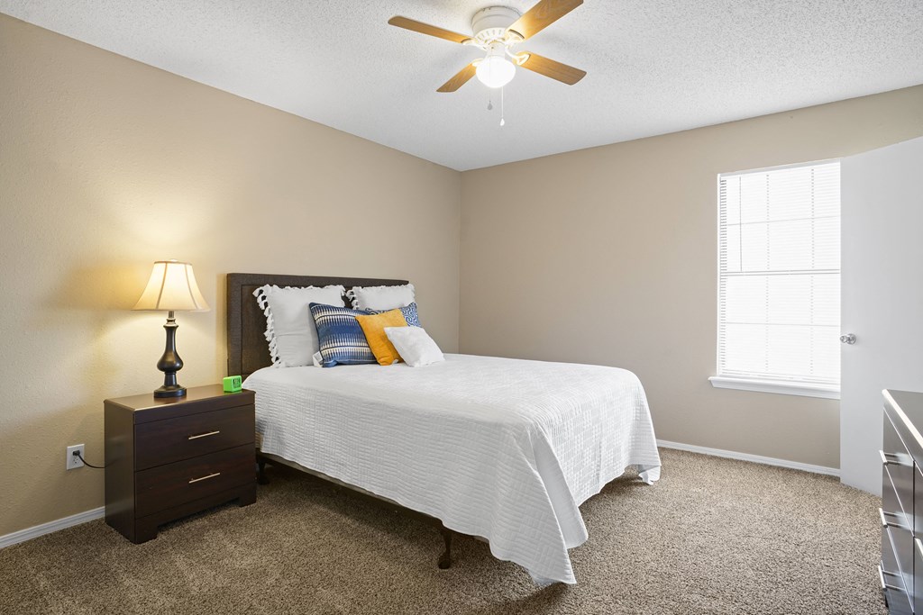 bed with white blanket and orange and blue pillows next to a window