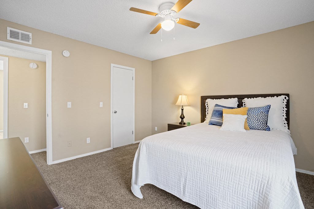 white bed with orange and blue pillows and fan above bed