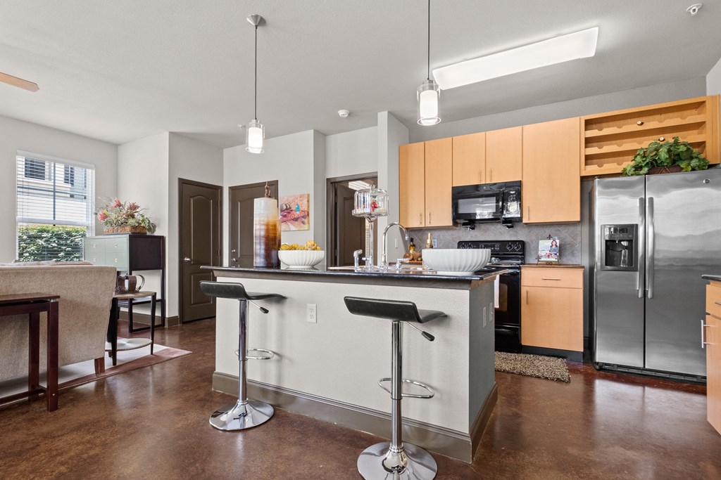 a kitchen with stainless steel appliances and an island with bar stools at The Millennium Towne Center Apartments, Baton Rouge, LA