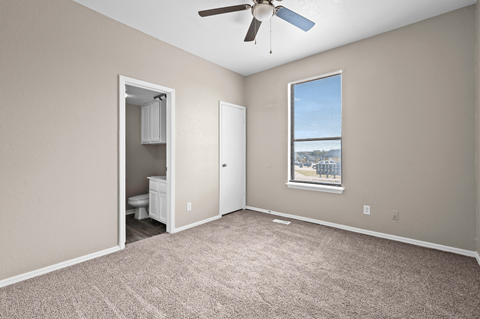 A room with a ceiling fan and a window with a view of a fence and trees.