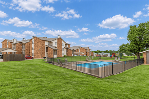 A large grassy area with a pool and apartment buildings in the background.