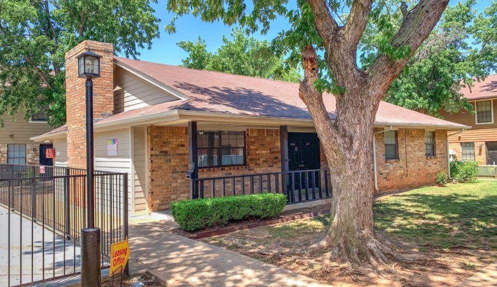 a small brick house with a tree and a wrought iron fence