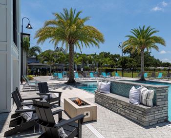 A pool area with a fire pit and lounge chairs at The Addison on Long Bayou Apartments, Seminole, FL