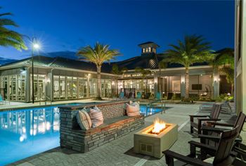 A poolside area with a lit fire pit and lounge chairs at The Addison on Long Bayou Apartments, Seminole, FL, 33772