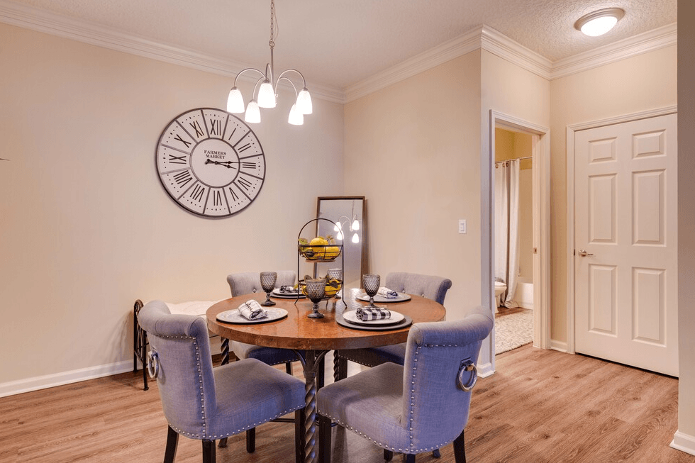 a dining room with a table and chairs and a clock on the wall at Magnolia Village Apartments, Florida 32207