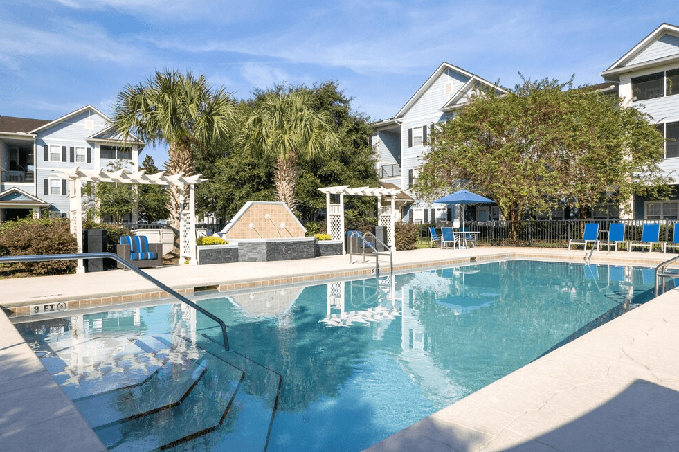 a swimming pool with blue chaise lounge chairs and palm trees in the background at Magnolia Village Apartments, Jacksonville, FL