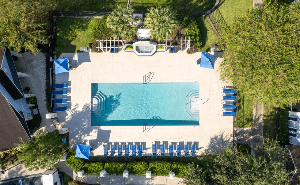 arial view of a swimming pool with chaise lounge chairs and trees in the background at Magnolia Village Apartments, Jacksonville, Florida