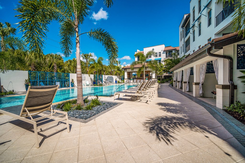 a pool with chairs and palm trees next to a building at Magnolia Square, Naples, FL