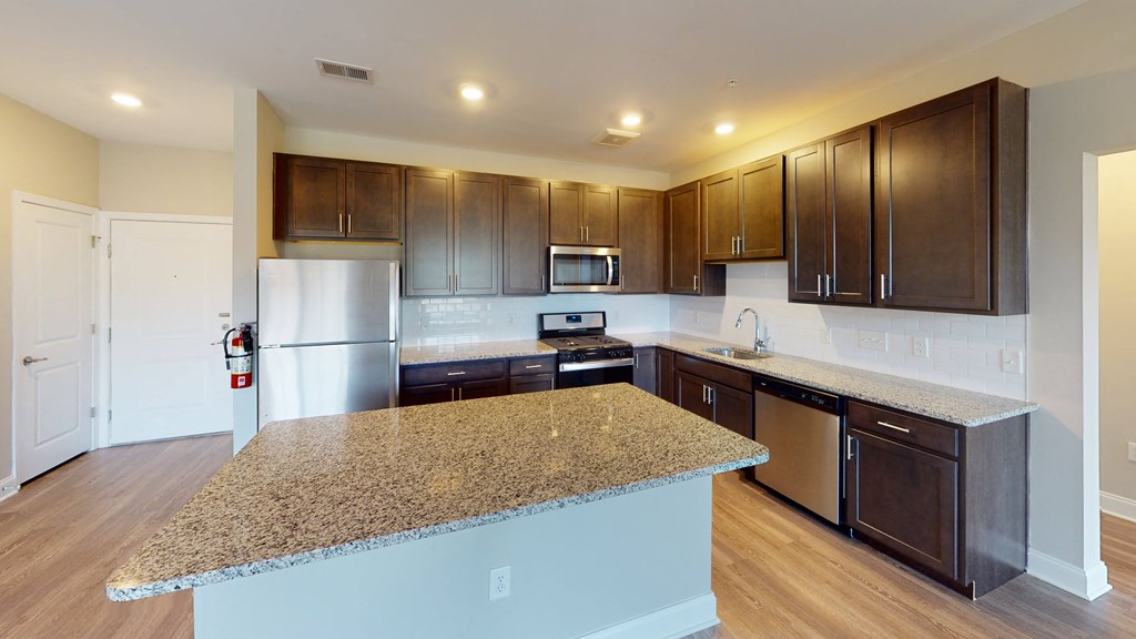 a kitchen with dark wood cabinets and an island with granite countertops at The Landing Apartments, Hazlet, NJ