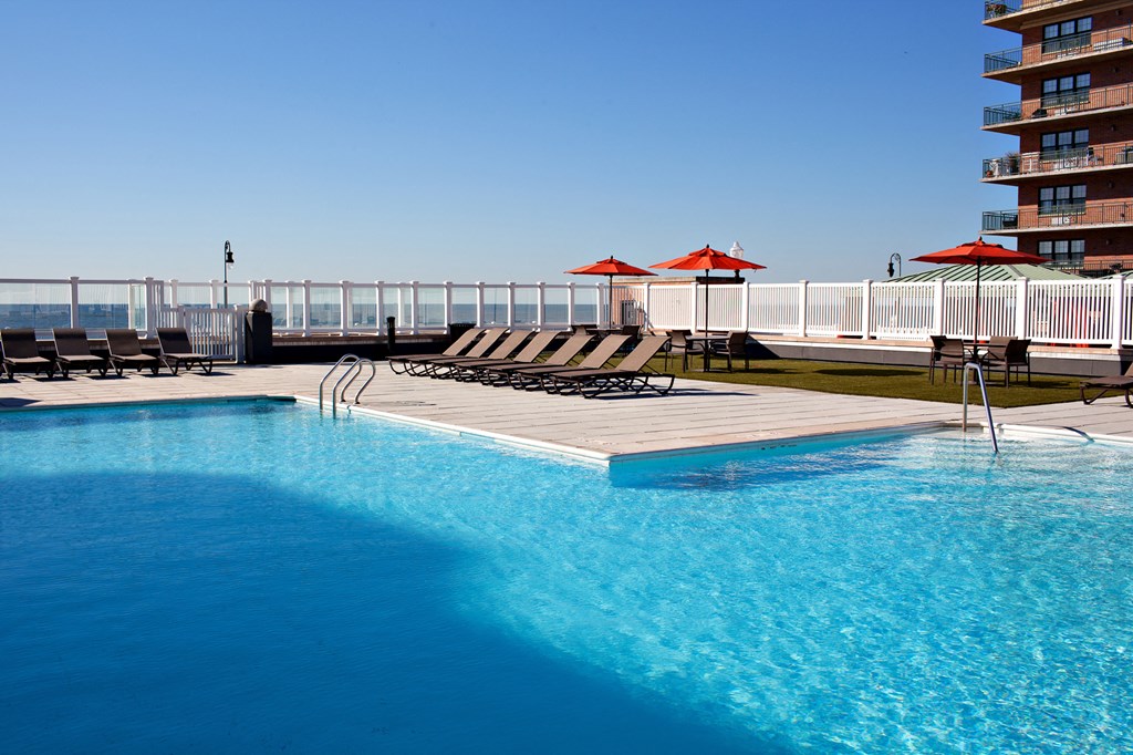 a swimming pool with chairs and umbrellas next to a hotel at 10 West Apartments, Long Beach, NY