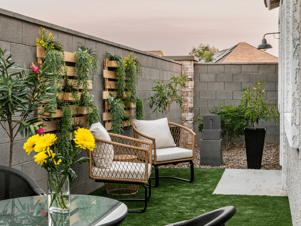 a backyard patio with two chairs and a table and a vase of flowers