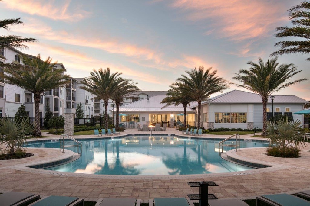 A large swimming pool surrounded by palm trees and a building in the background at Enclave at 3230 Apartments, South Daytona, FL, 32119