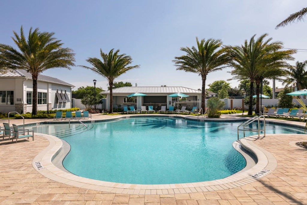 A large swimming pool surrounded by palm trees and lounge chairs at Enclave at 3230 Apartments, South Daytona, FL