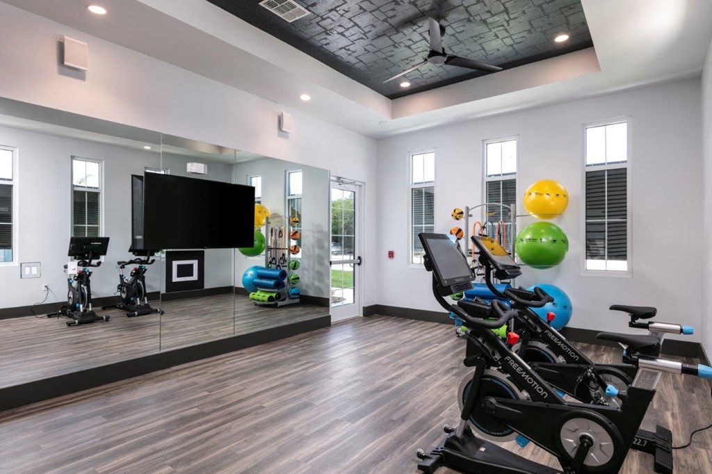 A room with a wooden floor and a ceiling fan, equipped with exercise bikes and a television at Enclave at 3230 Apartments, South Daytona, FL