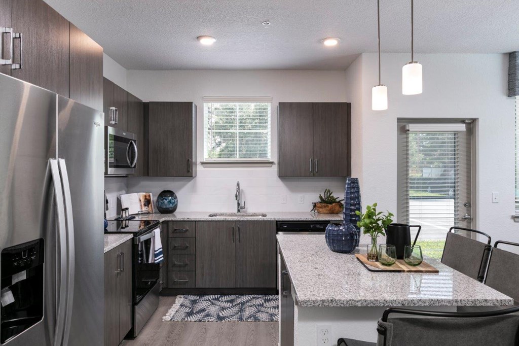 A modern kitchen with a stainless steel refrigerator and dark wood cabinets at Enclave at 3230 Apartments, South Daytona