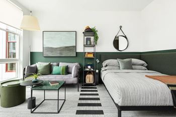 A bedroom with a bed, a couch, a table, and a plant.
