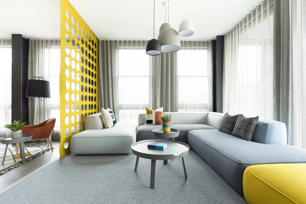 A modern living room with a grey sofa, a yellow accent, and a yellow and black geometric wall panel.