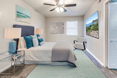 A bedroom with a bed, a ceiling fan, and a painting on the wall.