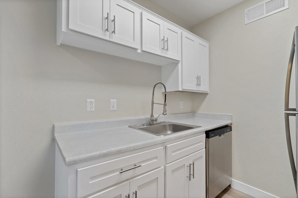 an empty kitchen with white cabinets and a sink and refrigerator