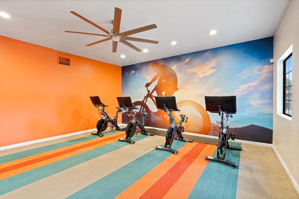Gym with exercise bikes and a mural of a man riding a bike at Verde Apartments in Tucson, AZ.