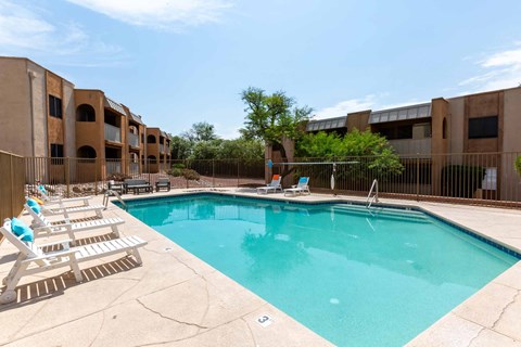 A swimming pool surrounded by sun loungers and apartment buildings.