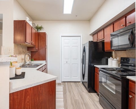 Kitchen with black appliances and wood cabinets at Park Hudson Place Apartments, Bryan, Texas
