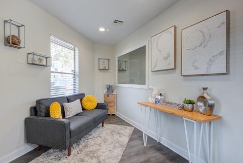 A grey couch with yellow pillows sits in a room with white walls and a white floor.