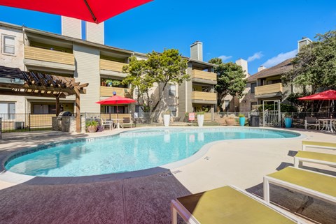 A swimming pool surrounded by a red umbrella and a building in the background.