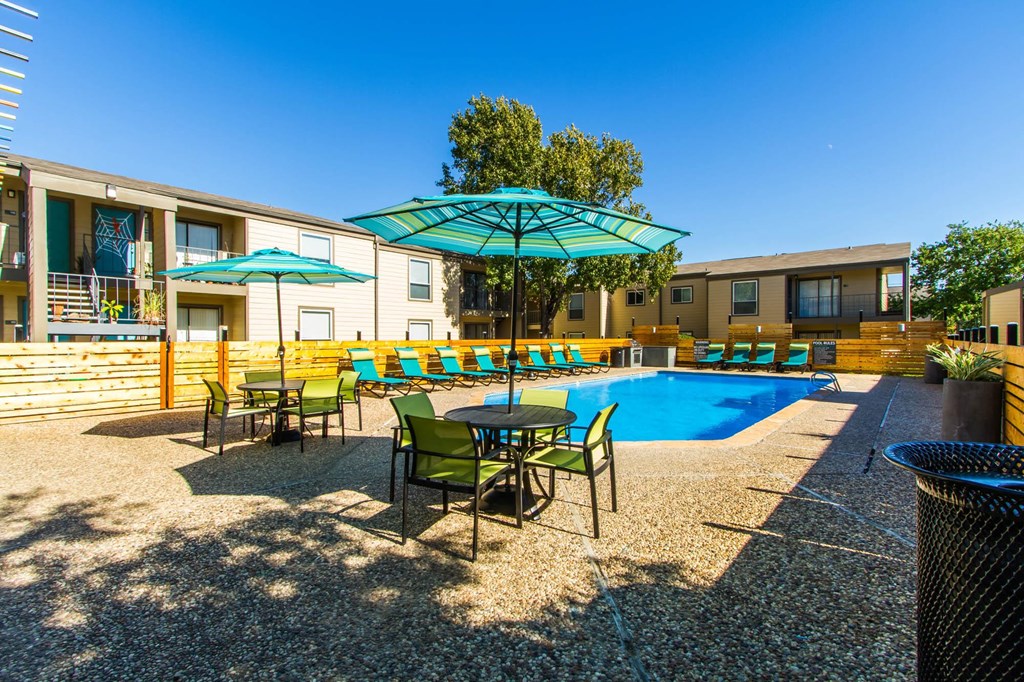 our apartments have a pool and patio with chairs and umbrellas at Sundance and Sausalito Apartments, College Station, TX