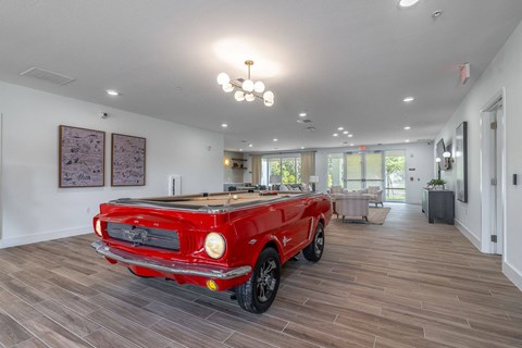 A red vintage car is parked in a spacious room with wood flooring.