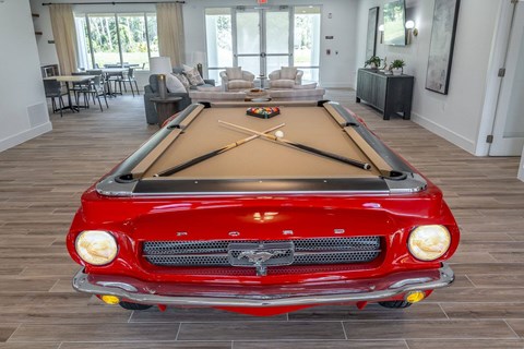 A red vintage car is parked in a room with a pool table.