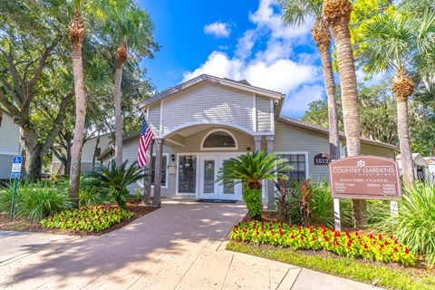 The image shows the front of a building with a sign that reads "Country Gardens" and a flag hanging from the entrance.