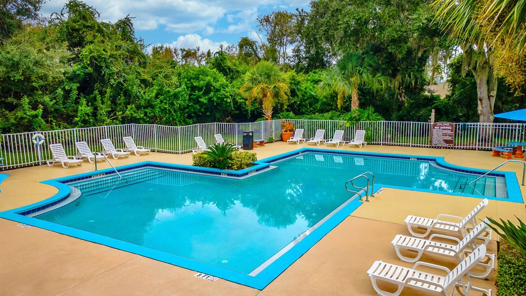 A large outdoor swimming pool surrounded by trees and lounge chairs.