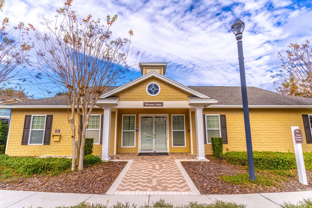 A yellow house with a brown roof and a tree in front.